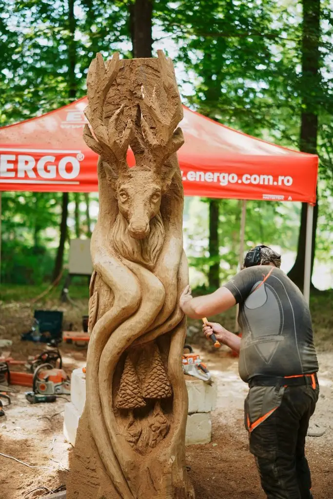Sculptor lucrând cu drujba un basorelief cu cerb, la concursul de sculptură al festivalului