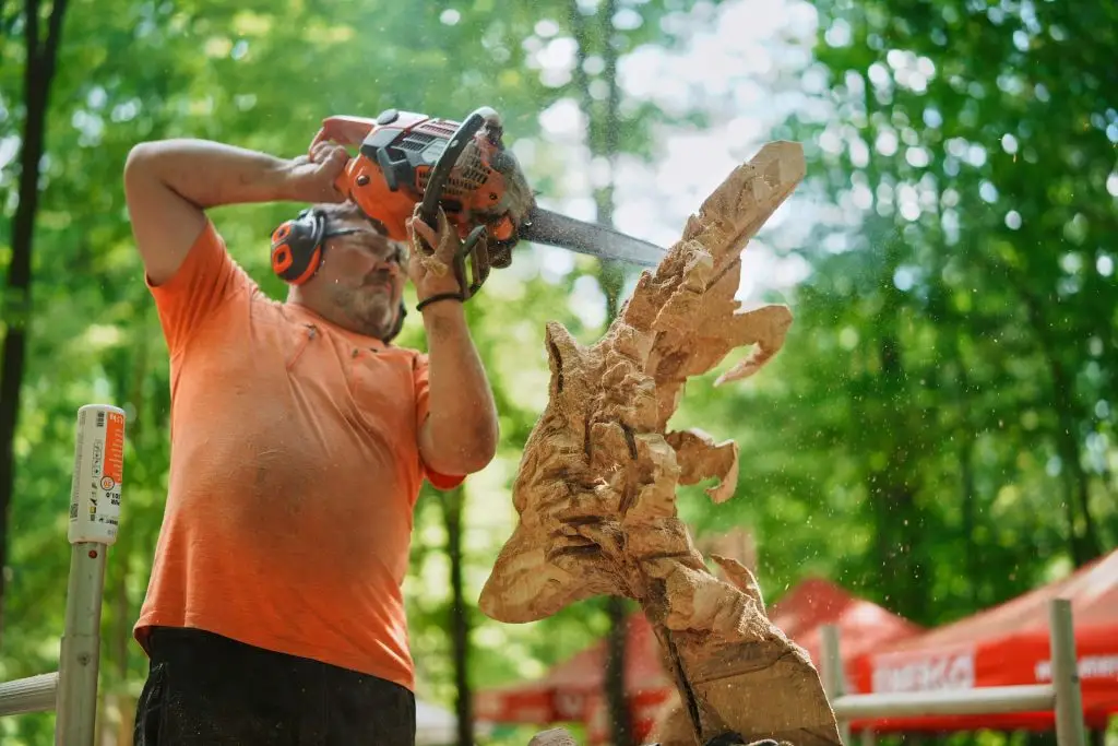 Sculptor în plin lucru, cu rumeguș în aer, la concursul de sculptură în lemn